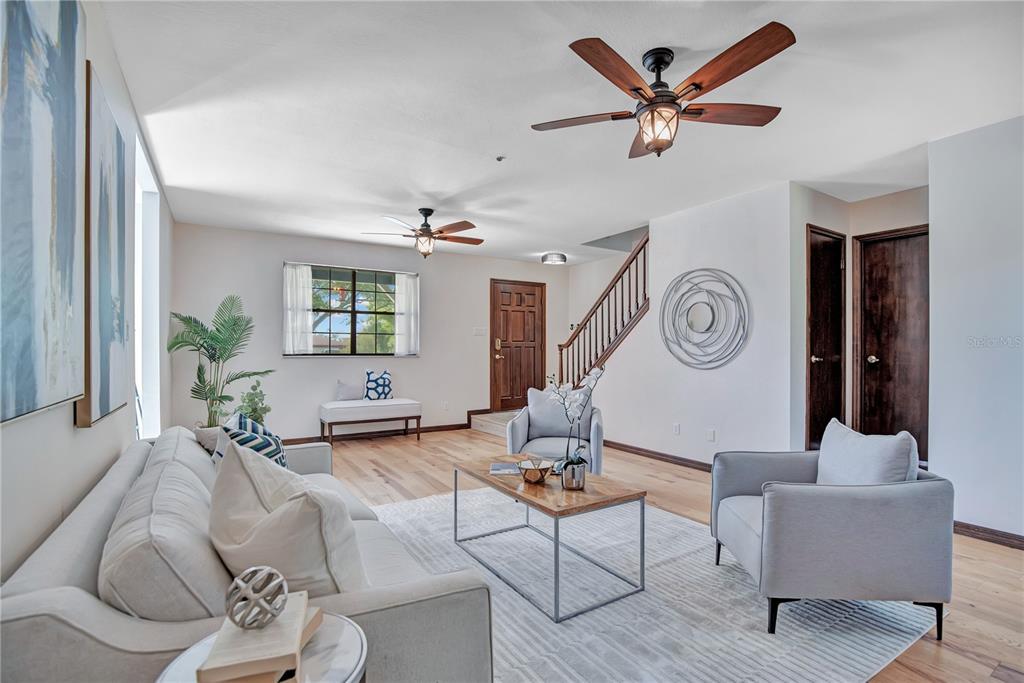 A living room features light hardwood floors, two ceiling fans, and a staircase with wood railings — 1898 ODHAM DRIVE, DELTONA, FL