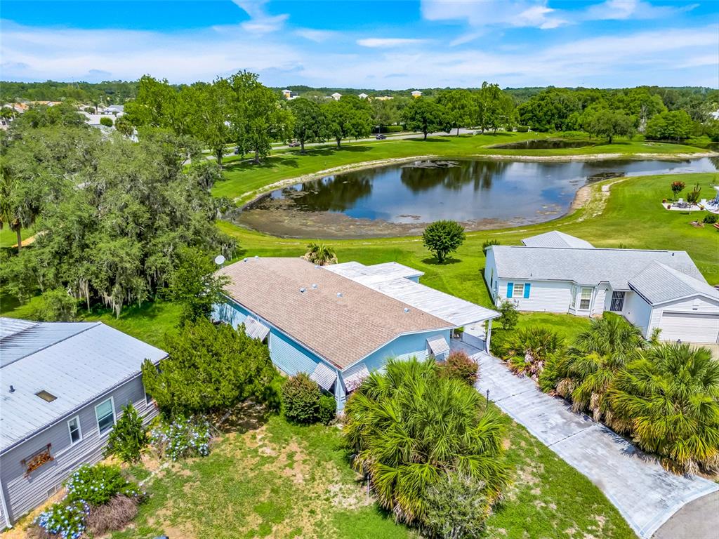An aerial view shows a light blue house with a brown roof near a pond — 25224 WILD HERON, LEESBURG, FL