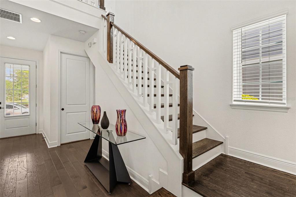 A foyer features dark wood flooring, a glass console table, and a staircase with wooden treads — 8274 NEMOURS PARKWAY, ORLANDO, FL