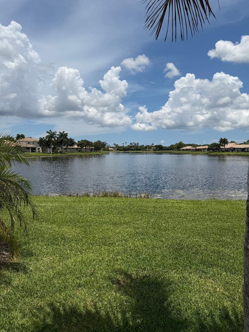 A view of a lake surrounded by houses and palm trees under a cloudy sky — 2332 Curley Cut, Royal Palm Beach FL 33411, ROYAL PALM BEACH, FL