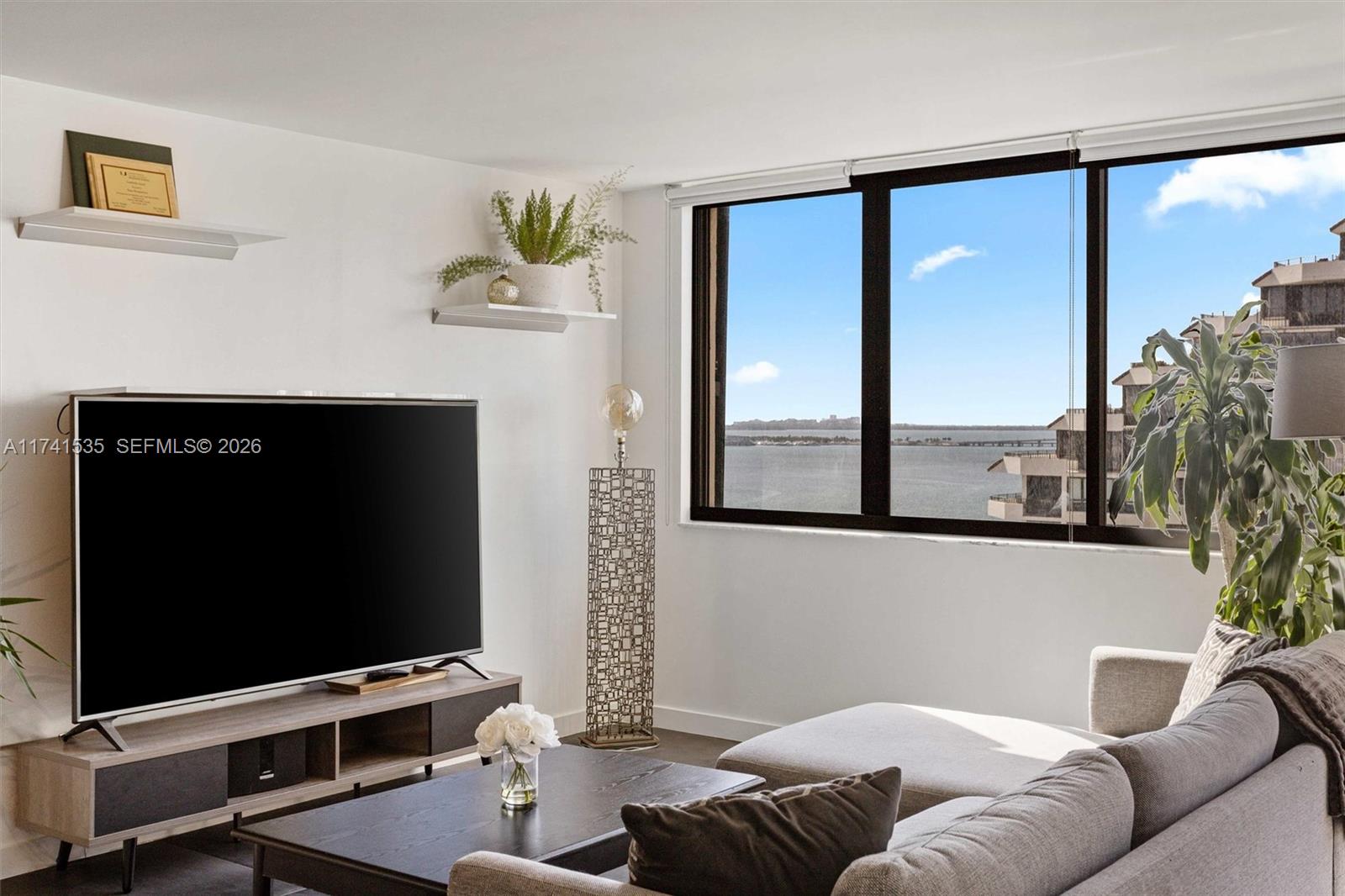 A living room features a television, a gray sofa, and a large window overlooking water — 540 Brickell Key Dr # 1519, Miami FL 33131, MIAMI, FL