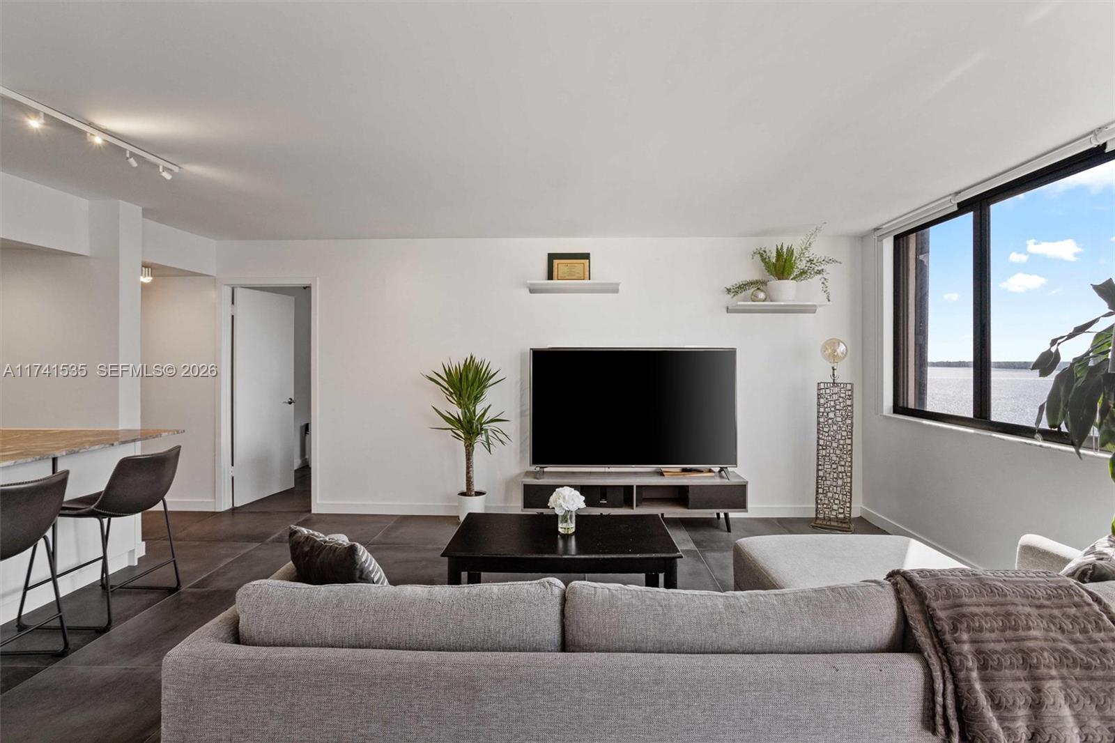 A living room features a grey sofa, a television on a console, and a water view — 540 Brickell Key Dr # 1519, Miami FL 33131, MIAMI, FL