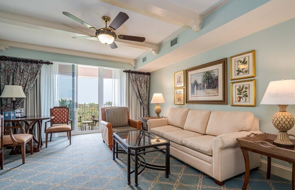 A living room with a beige sofa, patterned carpet, ceiling fan, and sliding glass balcony doors — 200 OCEAN CREST DRIVE UNIT 325, PALM COAST, FL