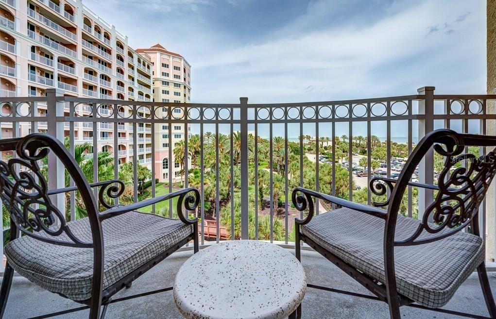 A balcony with two metal chairs and a small table overlooking palm trees and buildings — 200 OCEAN CREST DRIVE UNIT 325, PALM COAST, FL