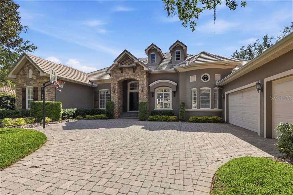 A covered patio with stone pavers overlooks a swimming pool with a rock waterfall feature — 6102 S HAMPSHIRE COURT, WINDERMERE, FL