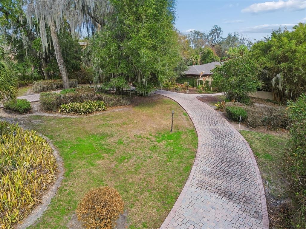 A paved brick walkway curves through a grassy yard toward a house surrounded by trees — 5324 WOODHAVEN LANE, LAKELAND, FL
