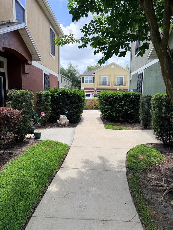 A concrete walkway leads between two multi-story residential buildings toward a yellow house in the distance — 1521 SAN JACINTO CIRCLE, SANFORD, FL
