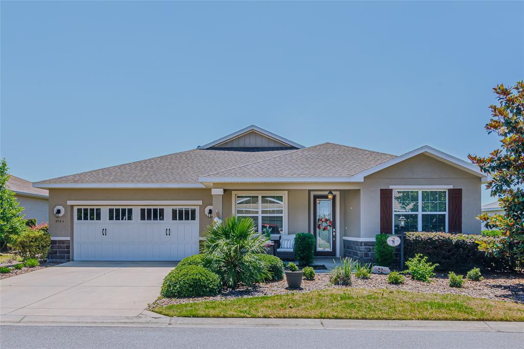 A single-story suburban house with a two-car garage, tan stucco siding, and landscaped front yard — 9985 SW 88TH LOOP, OCALA, FL