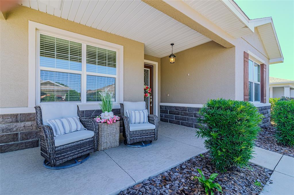 A covered front porch features two wicker chairs, a small table, and stone veneer accents — 9985 SW 88TH LOOP, OCALA, FL