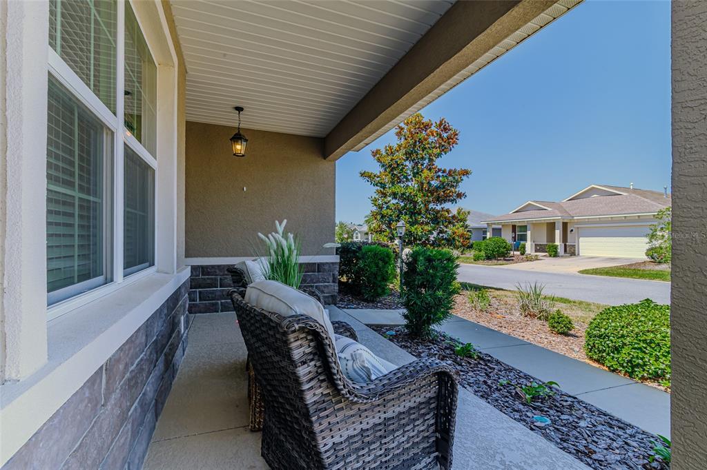 A covered front porch features wicker chairs, stone siding, and a view of the street — 9985 SW 88TH LOOP, OCALA, FL