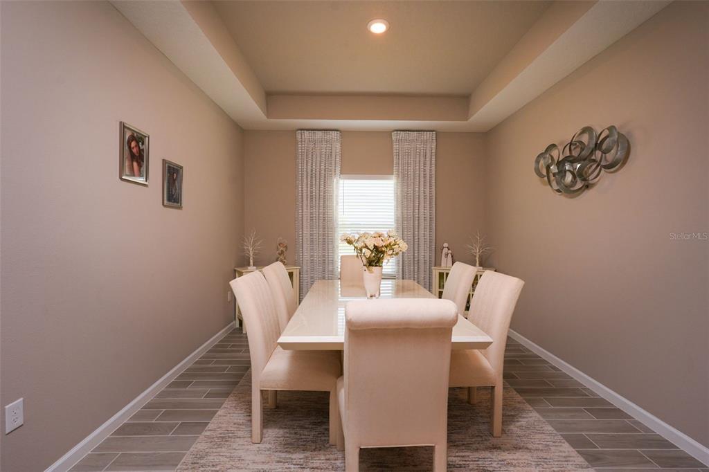 A dining room features a tray ceiling, light-colored furniture, and gray tile flooring — 9332 SW 58TH CIRCLE, OCALA, FL