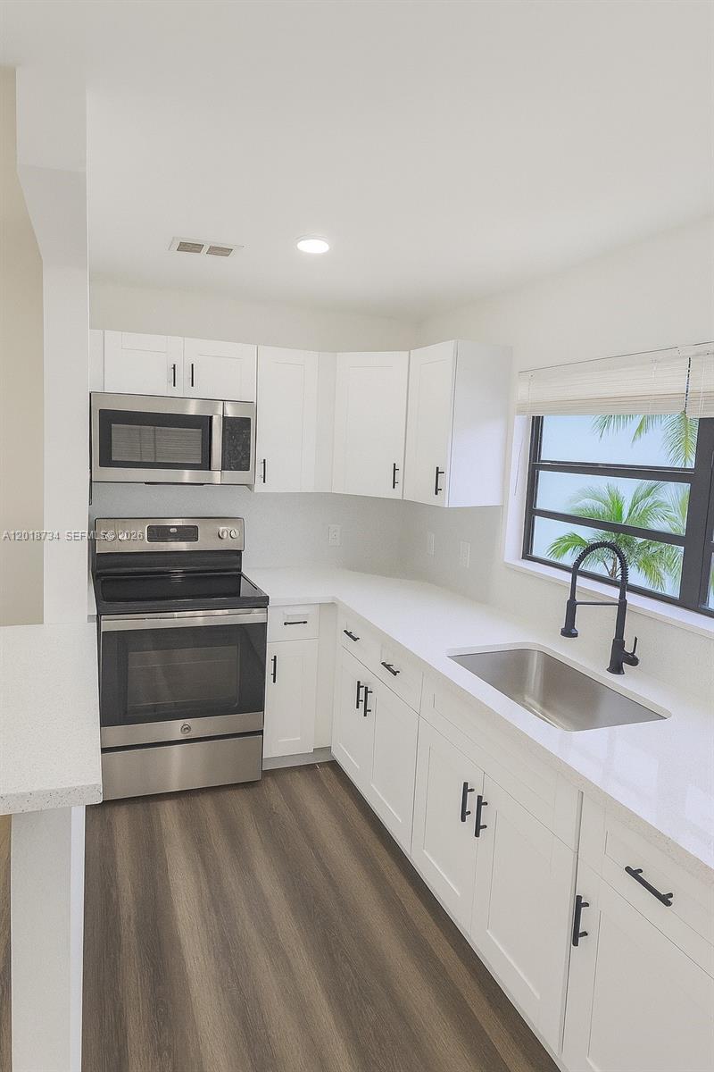 A kitchen features white cabinets, stainless steel appliances, a sink, and wood-look flooring — 417 NW 2nd Ave # 9, Hallandale Beach FL 33009, HALLANDALE BEACH, FL