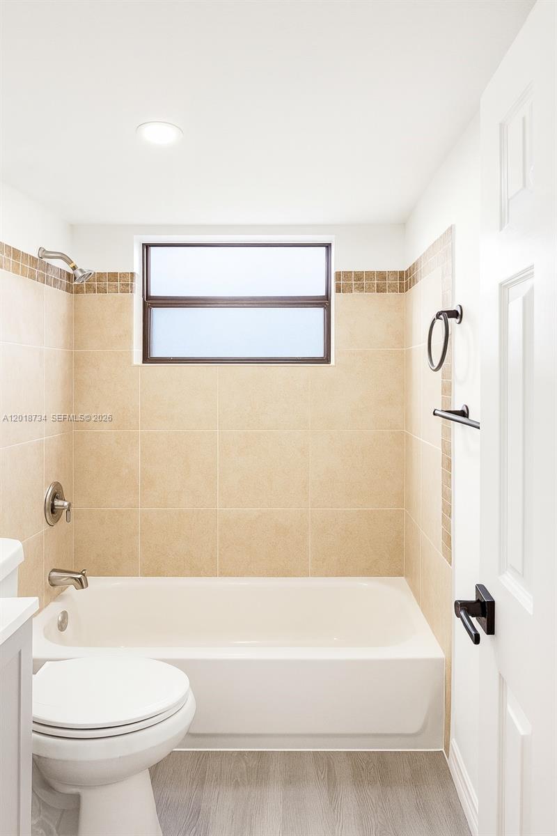 A bathroom features a white bathtub, beige tiled walls with a decorative border, and a window — 417 NW 2nd Ave # 9, Hallandale Beach FL 33009, HALLANDALE BEACH, FL