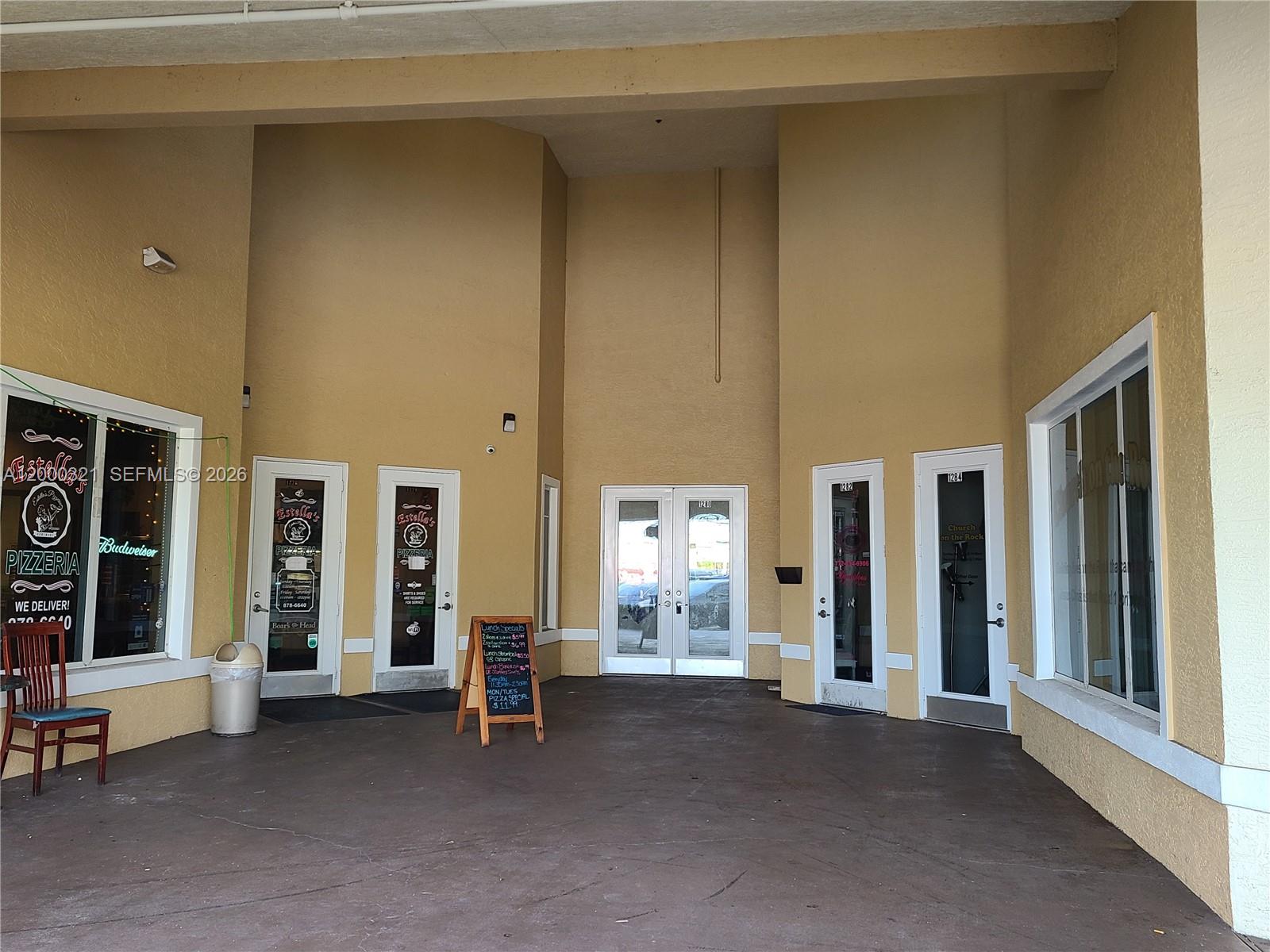 The exterior entrance of a commercial building features multiple glass doors and a pizzeria storefront — 1264 SW California Blvd # 1282, FL 34953, FL