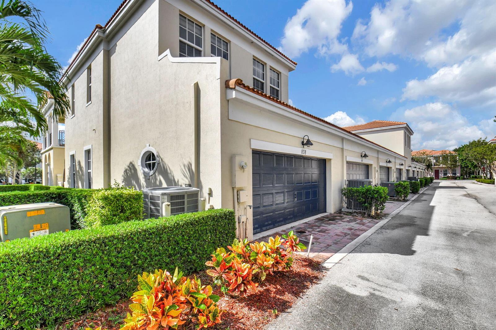 A beige two-story townhouse features a dark garage door and a landscaped front yard — 838 NW 83rd Lane, Boca Raton FL 33487, BOCA RATON, FL