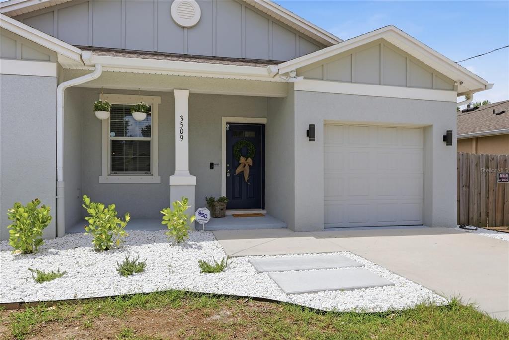 A single-story house exterior features a gray facade, a dark blue front door, and white gravel — 3509 E 10TH AVENUE, TAMPA, FL