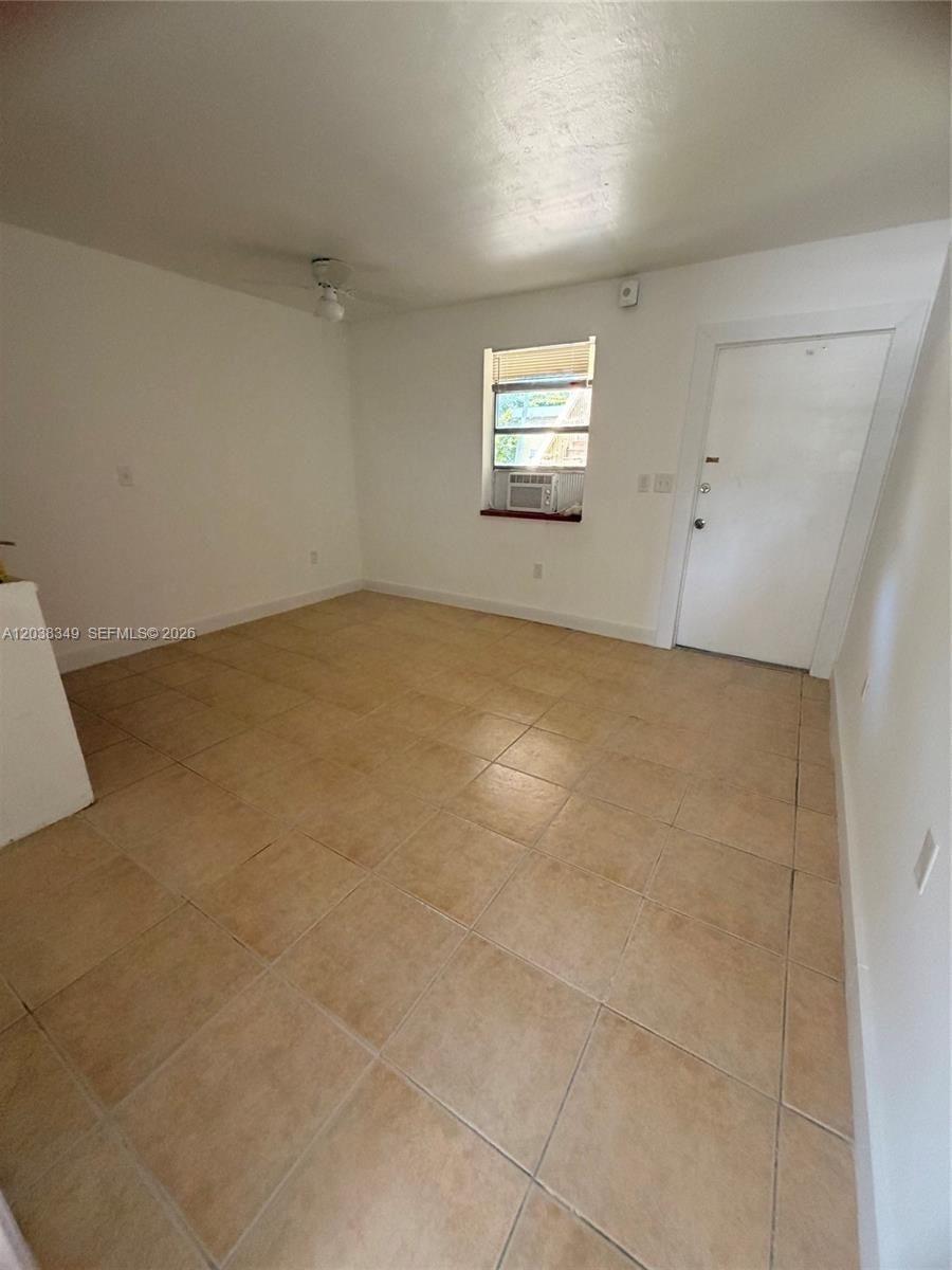 An empty room features light-colored tile flooring, white walls, a window, and a white door — 8450 NE Miami Ct # 4, Miami FL 33138, MIAMI, FL