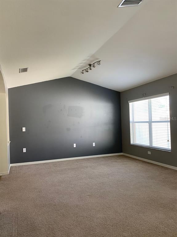 An empty room features a dark gray accent wall, beige carpeting, and a vaulted ceiling — 11355 FLORA SPRINGS DRIVE, RIVERVIEW, FL