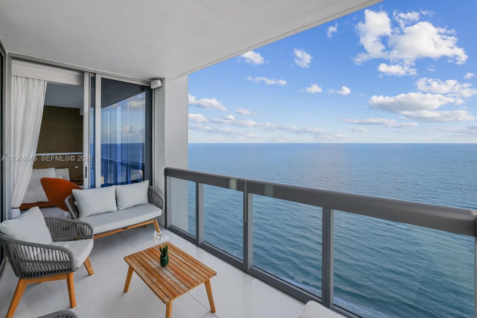 A balcony with outdoor furniture overlooks the ocean through a glass railing — 6899 Collins Ave # 2208, Miami Beach FL 33141, MIAMI BEACH, FL