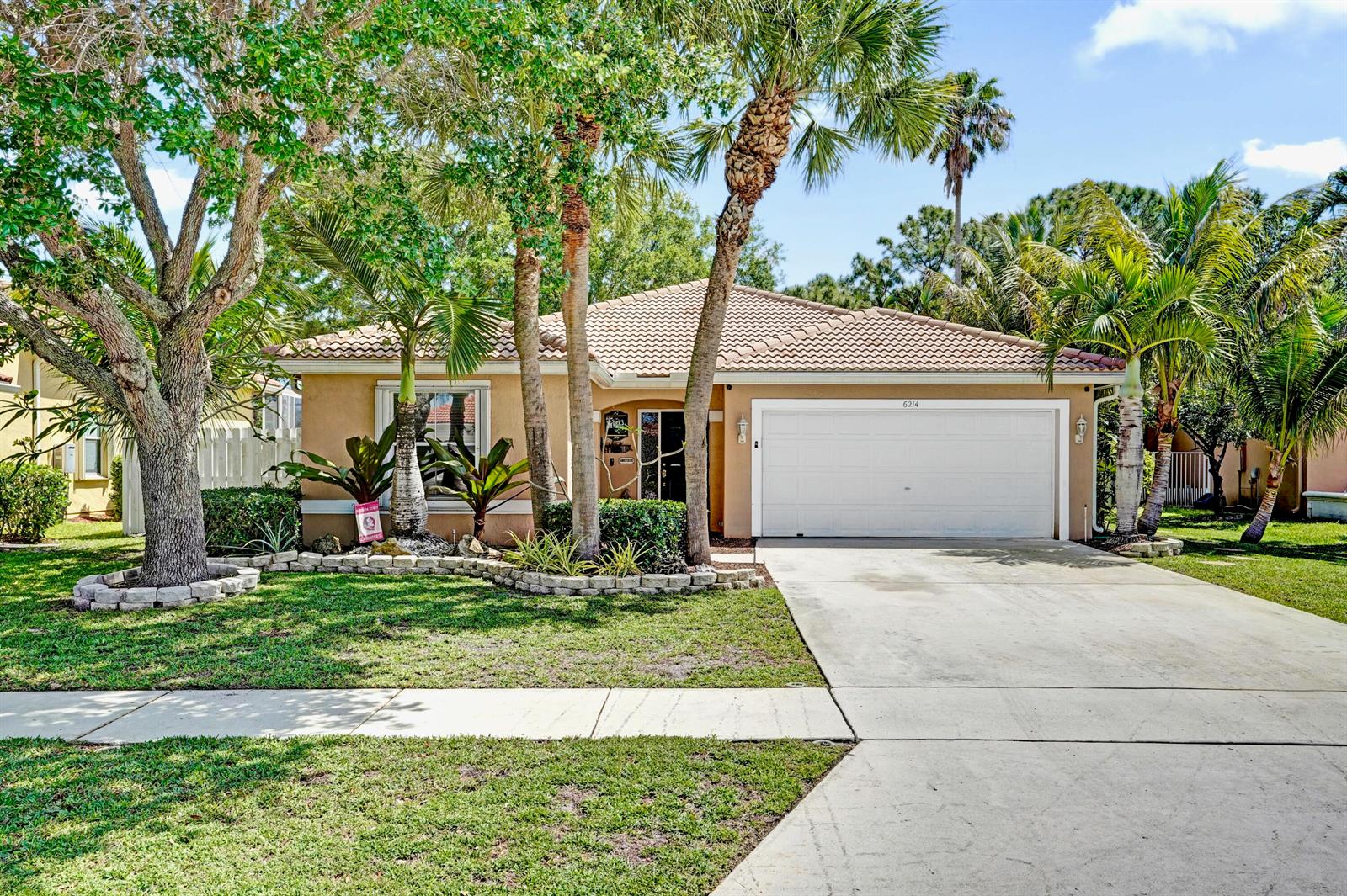 A single-story house with a tan stucco exterior, tile roof, and a two-car garage — 6214 Sand Hills Circle, Lake Worth FL 33463, LAKE WORTH, FL
