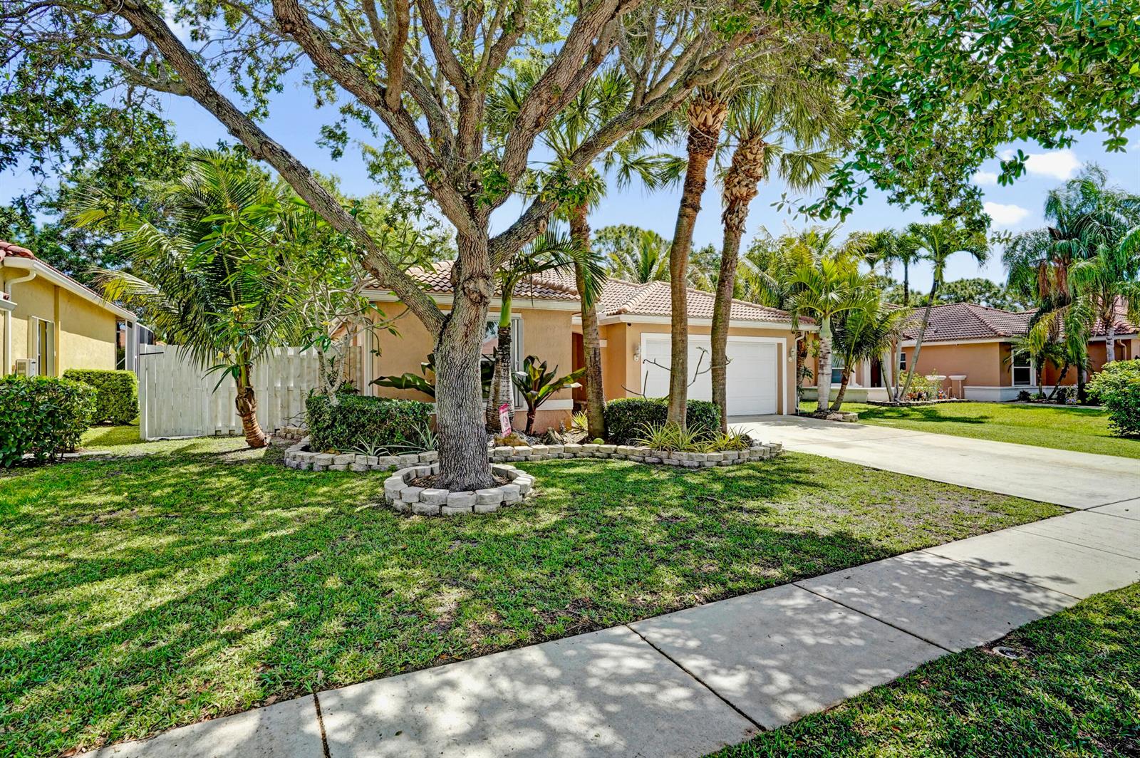 A single-story house with a tan exterior, a two-car garage, and a large front tree — 6214 Sand Hills Circle, Lake Worth FL 33463, LAKE WORTH, FL