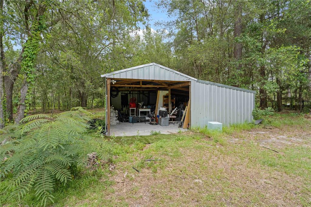 A metal-sided shed with an open front sits on a concrete slab in a wooded area — 9459 N EUBANKS TERRACE, DUNNELLON, FL