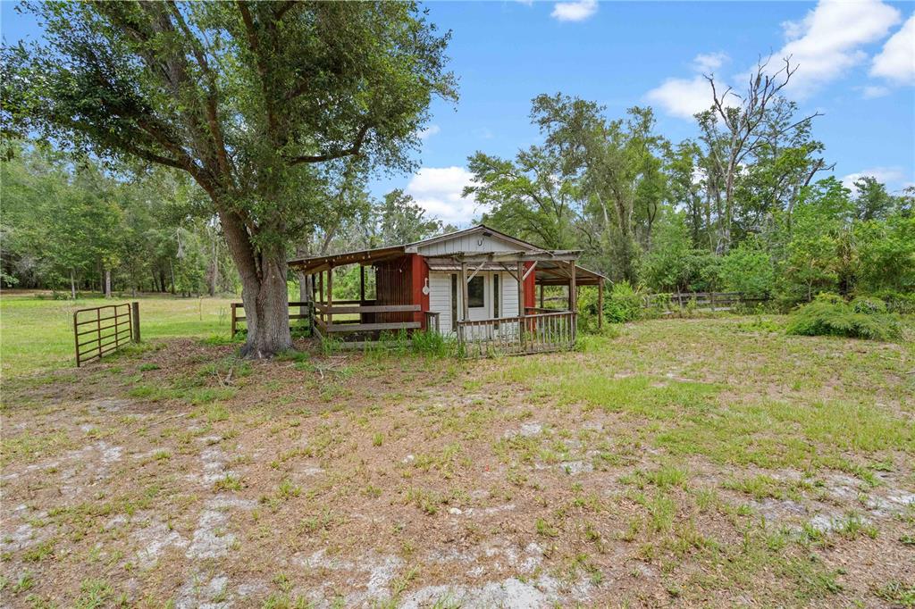 A small, weathered red and white shed sits in a grassy field under large trees — 9459 N EUBANKS TERRACE, DUNNELLON, FL
