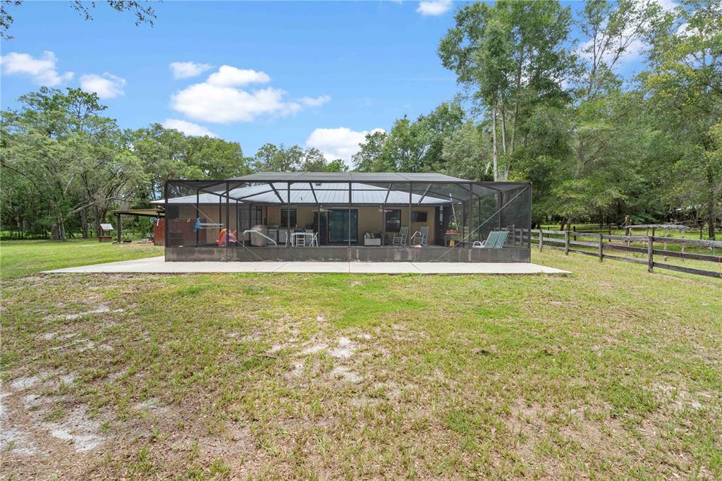A rear view of a house with a screened-in patio and a large grassy yard — 9459 N EUBANKS TERRACE, DUNNELLON, FL