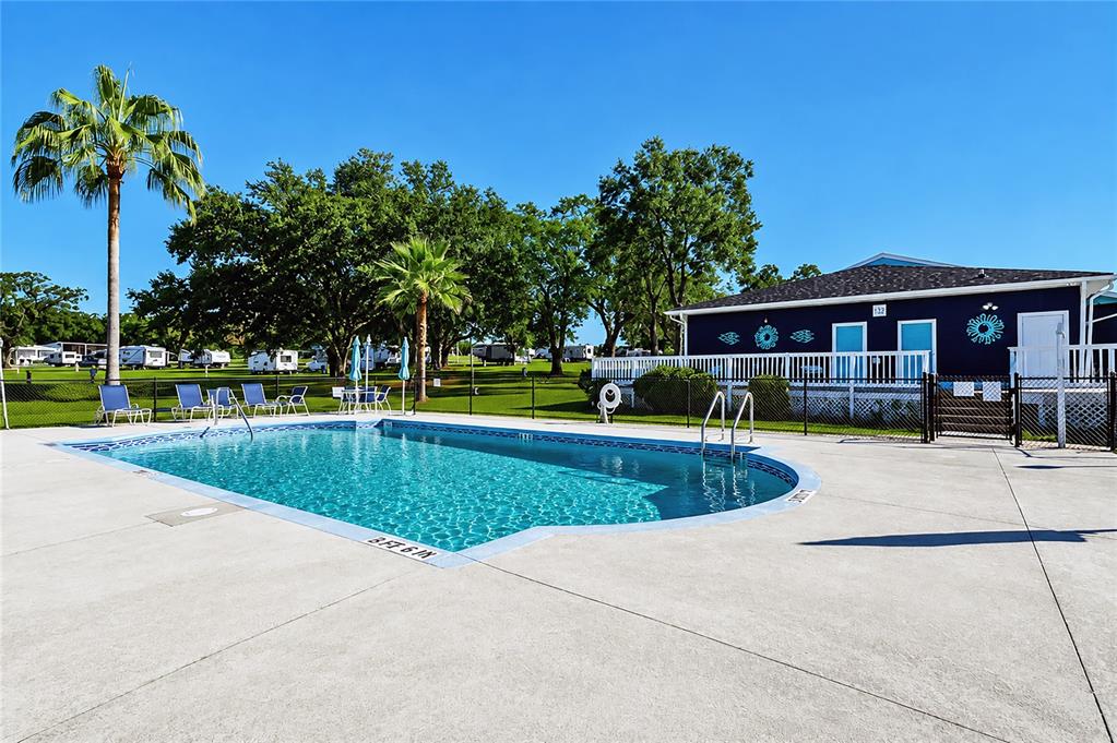 An outdoor swimming pool sits on a concrete patio next to a blue building — 10151 HAMP DRIVE, DADE CITY, FL