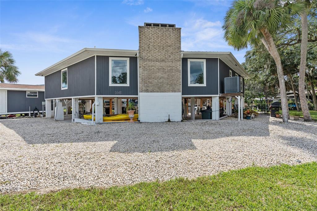 An elevated house with dark gray siding and a central brick chimney stands over gravel — 5648 S GARCIA ROAD, HOMOSASSA, FL