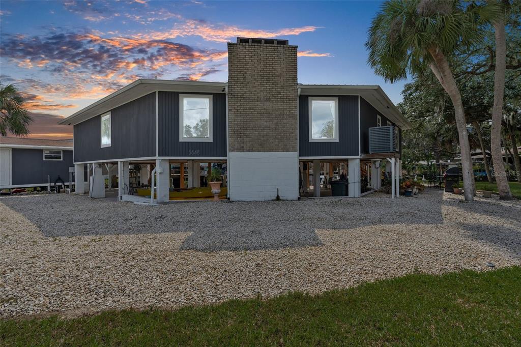 An elevated house with dark siding, a brick chimney, and a gravel yard at sunset — 5648 S GARCIA ROAD, HOMOSASSA, FL