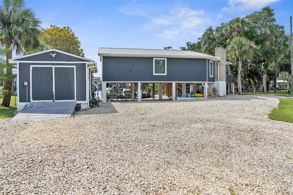 A stilt house with a gravel driveway and an attached shed under a blue sky — 5648 S GARCIA ROAD, HOMOSASSA, FL