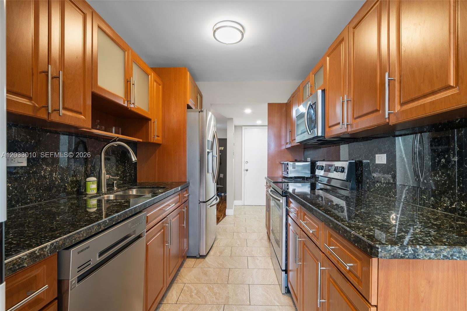 A galley kitchen features wood cabinets, dark granite countertops, and stainless steel appliances — 1690 NE 191st St # 1, Miami FL 33179, MIAMI, FL