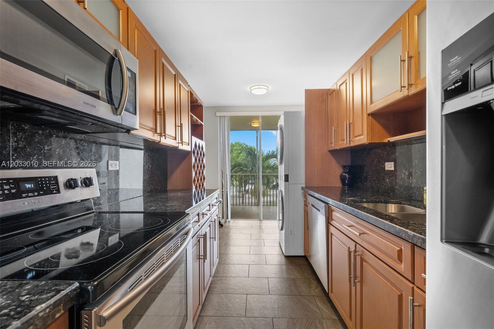 A galley kitchen features wood cabinets, black granite countertops, stainless steel appliances, and a balcony — 1690 NE 191st St # 1, Miami FL 33179, MIAMI, FL