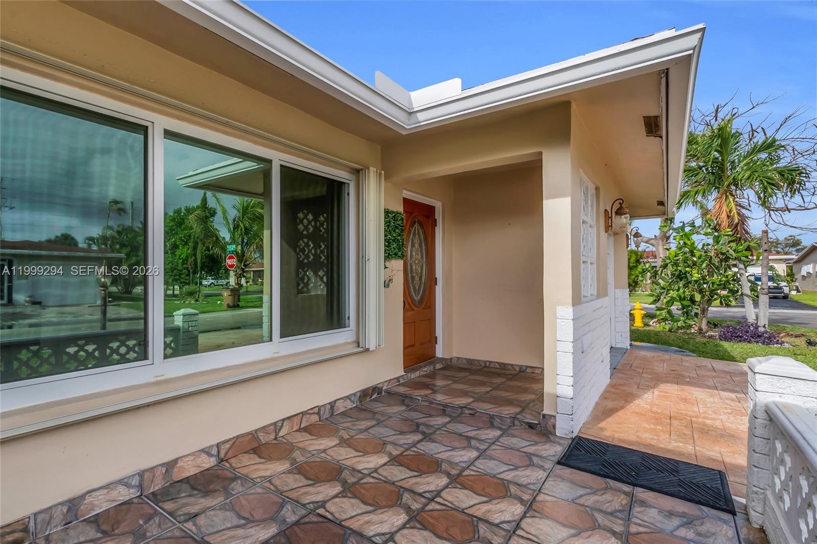 A covered front porch with patterned tile flooring leads to a wooden front door — 1280 NW 49th St, Deerfield Beach FL 33064, DEERFIELD BEACH, FL