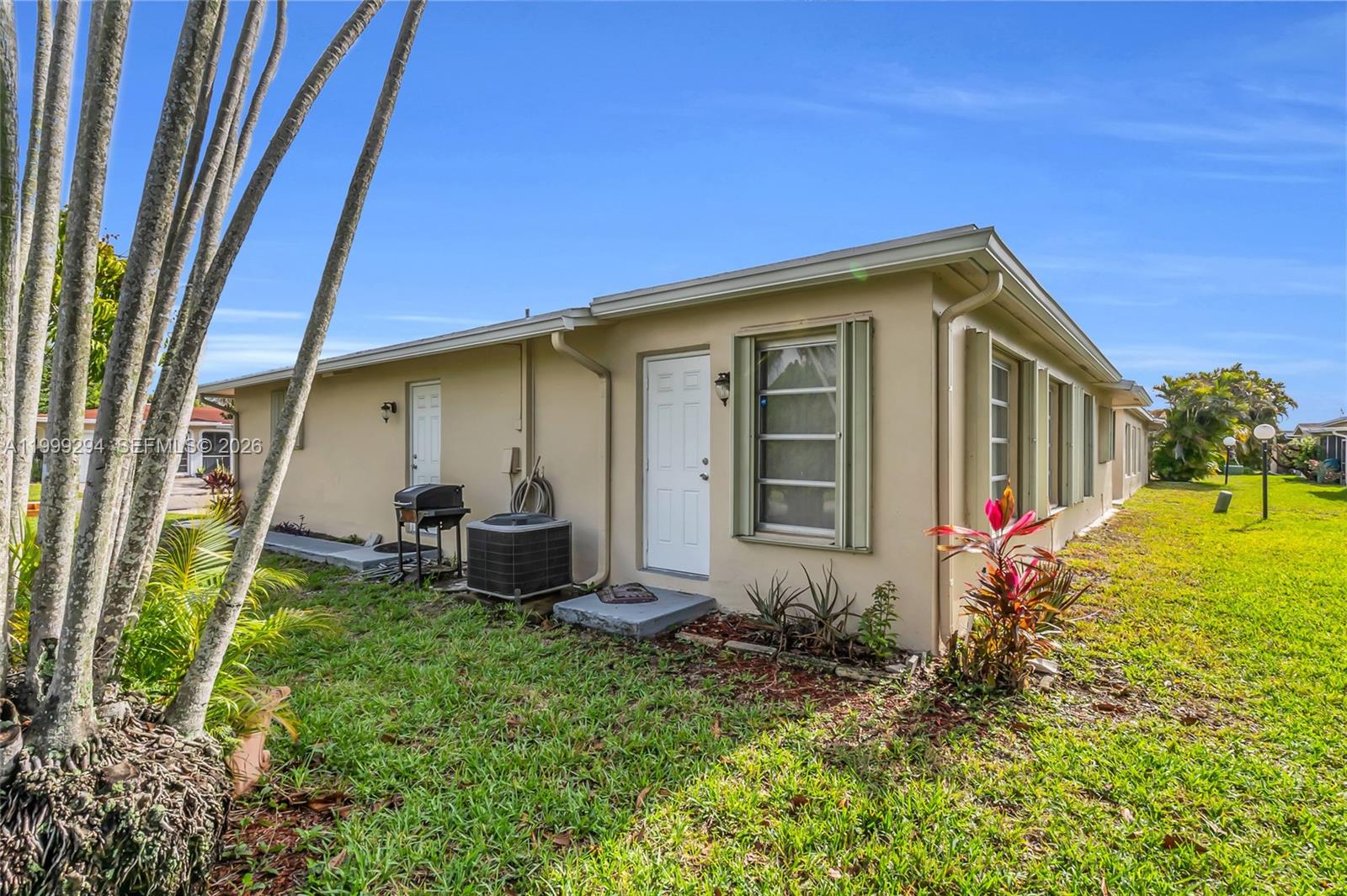 The exterior of a single-story beige house features a white door and an air conditioner — 1280 NW 49th St, Deerfield Beach FL 33064, DEERFIELD BEACH, FL