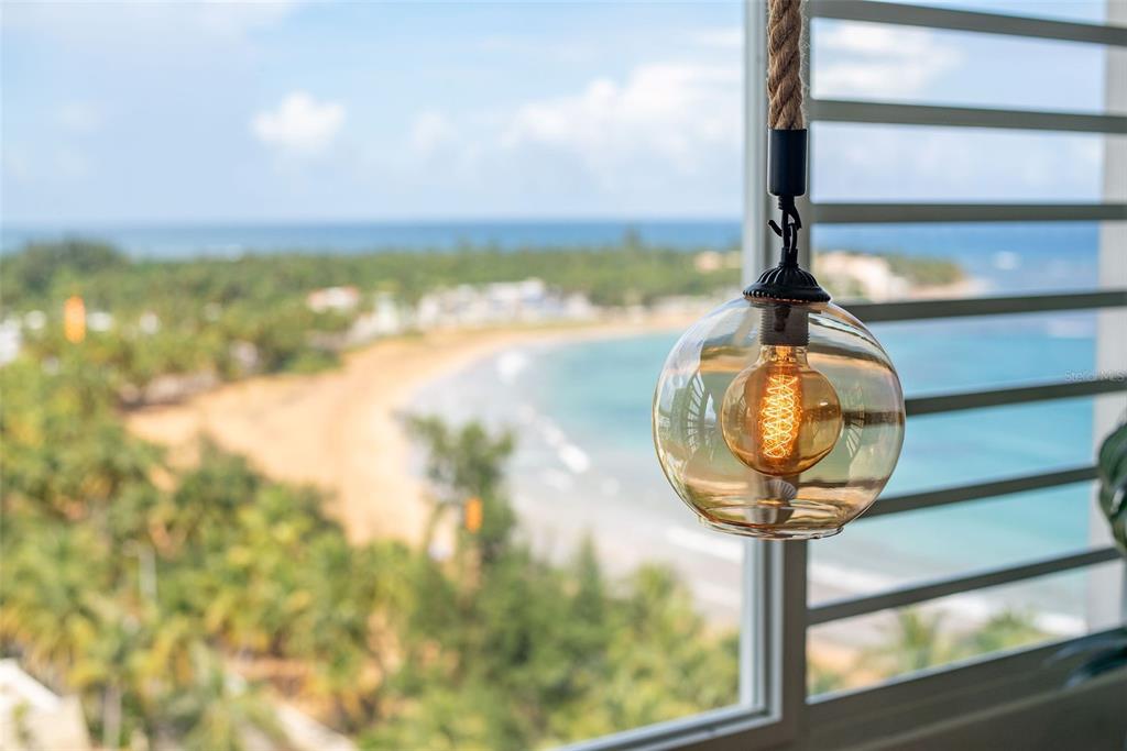 A pendant light with a rope cord hangs in front of a window overlooking a beach — 1404 COND PLAYA AZUL III UNIT 1404, LUQUILLO, PR