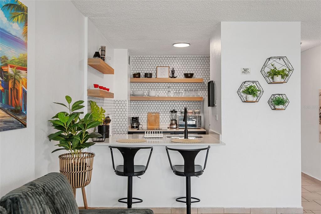 A kitchen features white hexagonal tile backsplashes, open wood shelving, and two black bar stools — 1404 COND PLAYA AZUL III UNIT 1404, LUQUILLO, PR