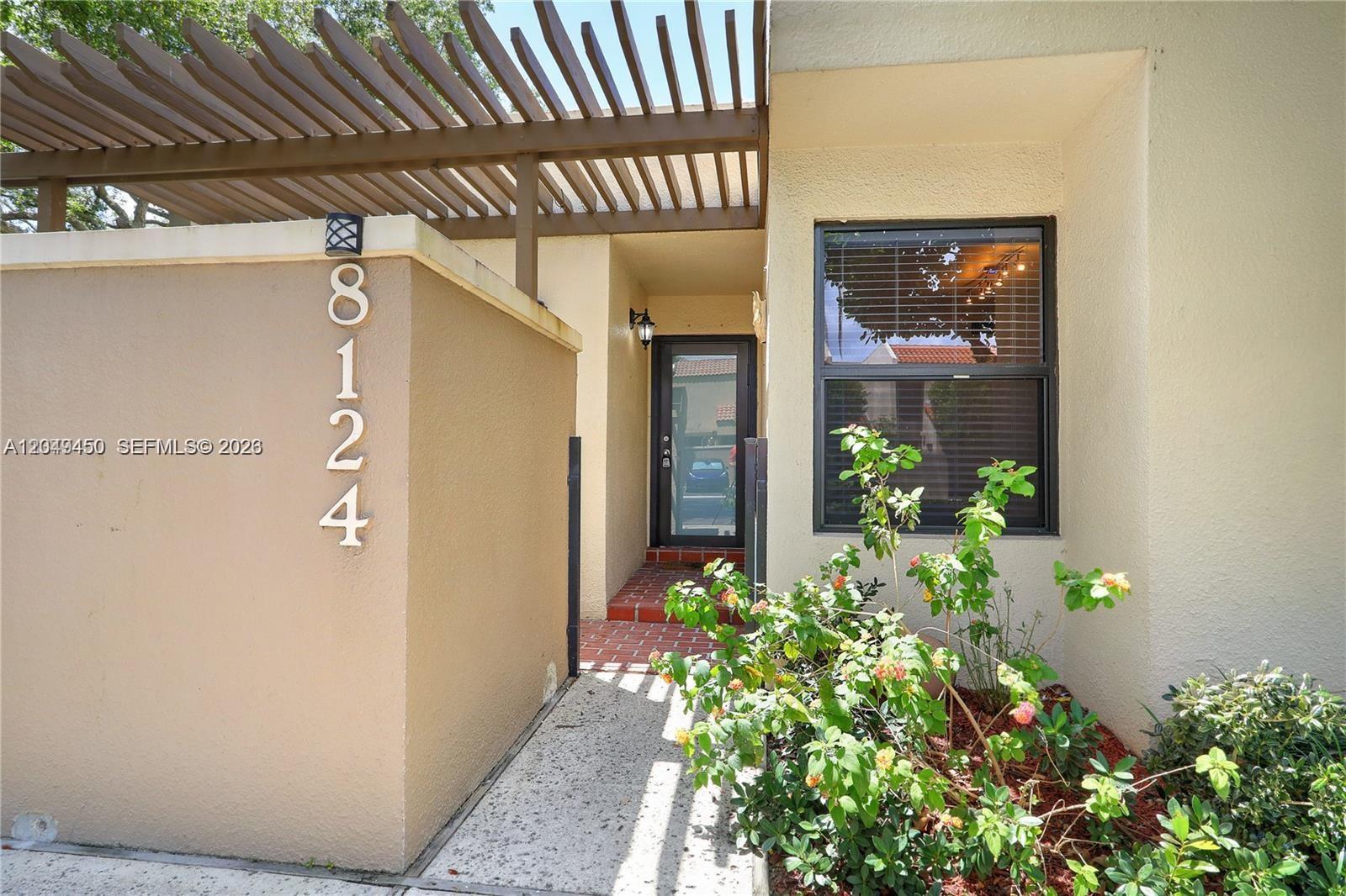 The exterior of a home features a tan stucco wall with house numbers and a pergola — 8124 SW 87th Ter, Miami FL 33143, MIAMI, FL