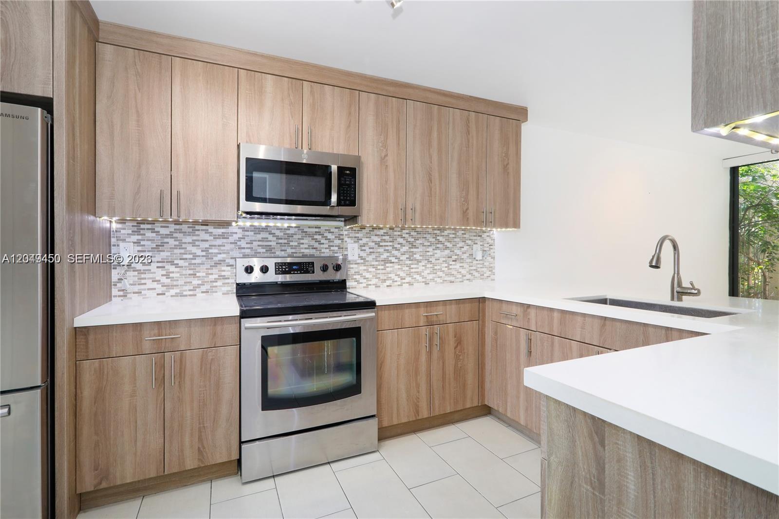 A modern kitchen features light wood cabinets, stainless steel appliances, and white countertops — 8124 SW 87th Ter, Miami FL 33143, MIAMI, FL