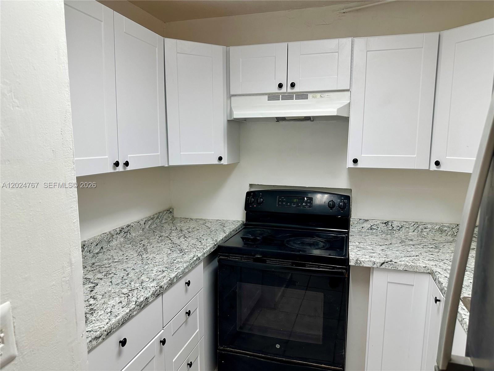 A kitchen features white shaker-style cabinets, granite countertops, and a black electric range — 6820 W Flagler St # 105, Miami FL 33144, MIAMI, FL