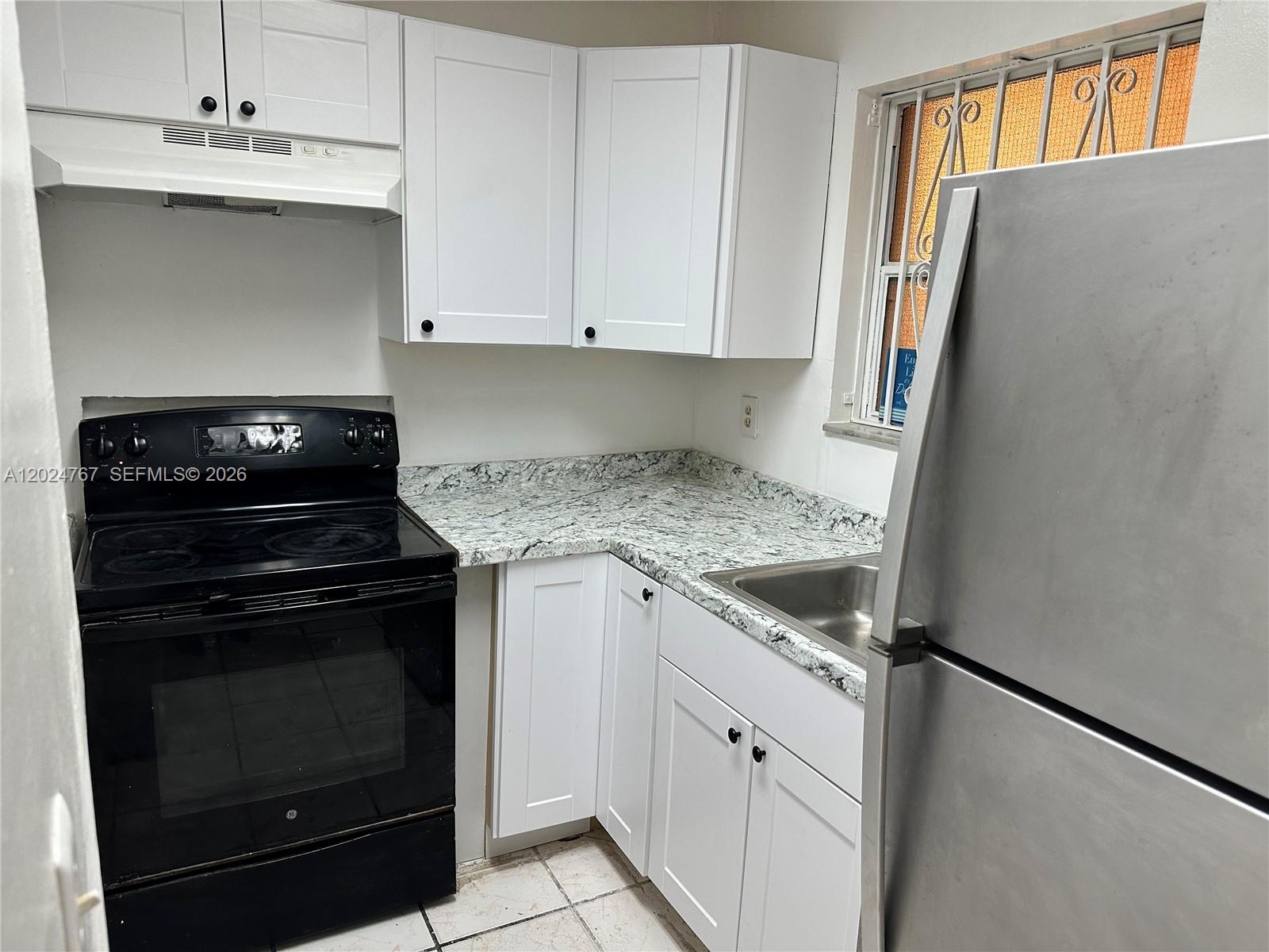 A kitchen features white cabinets, granite countertops, a black stove, and a stainless steel refrigerator — 6820 W Flagler St # 105, Miami FL 33144, MIAMI, FL