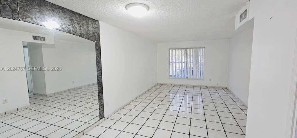 An empty room with white tiled floors, white walls, and a large mirrored accent wall — 6820 W Flagler St # 105, Miami FL 33144, MIAMI, FL