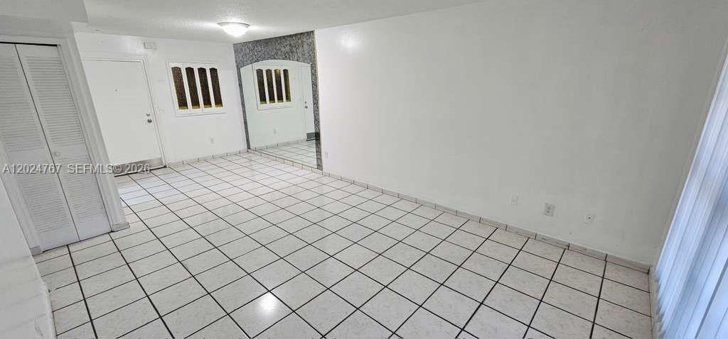 An empty room features white tiled floors, white walls, a closet, and a mirrored wall — 6820 W Flagler St # 105, Miami FL 33144, MIAMI, FL