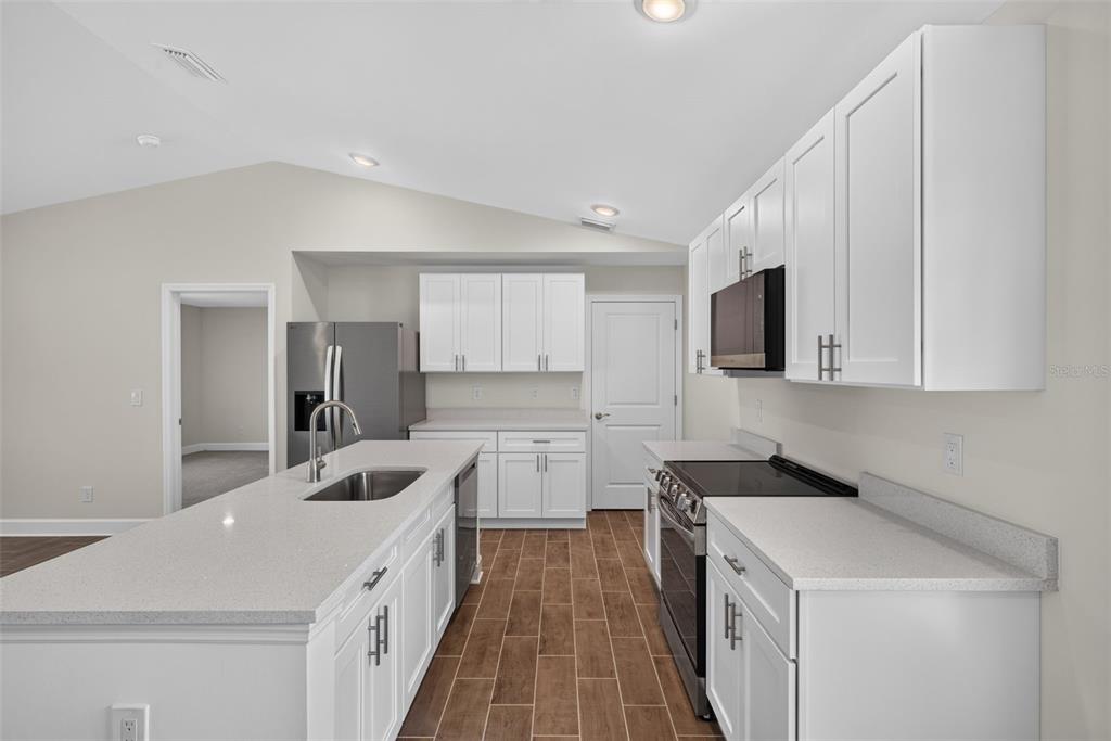 A kitchen features white cabinets, quartz countertops, a center island, and wood-look tile flooring — 3254 PLYMOUTH STREET, PORT CHARLOTTE, FL