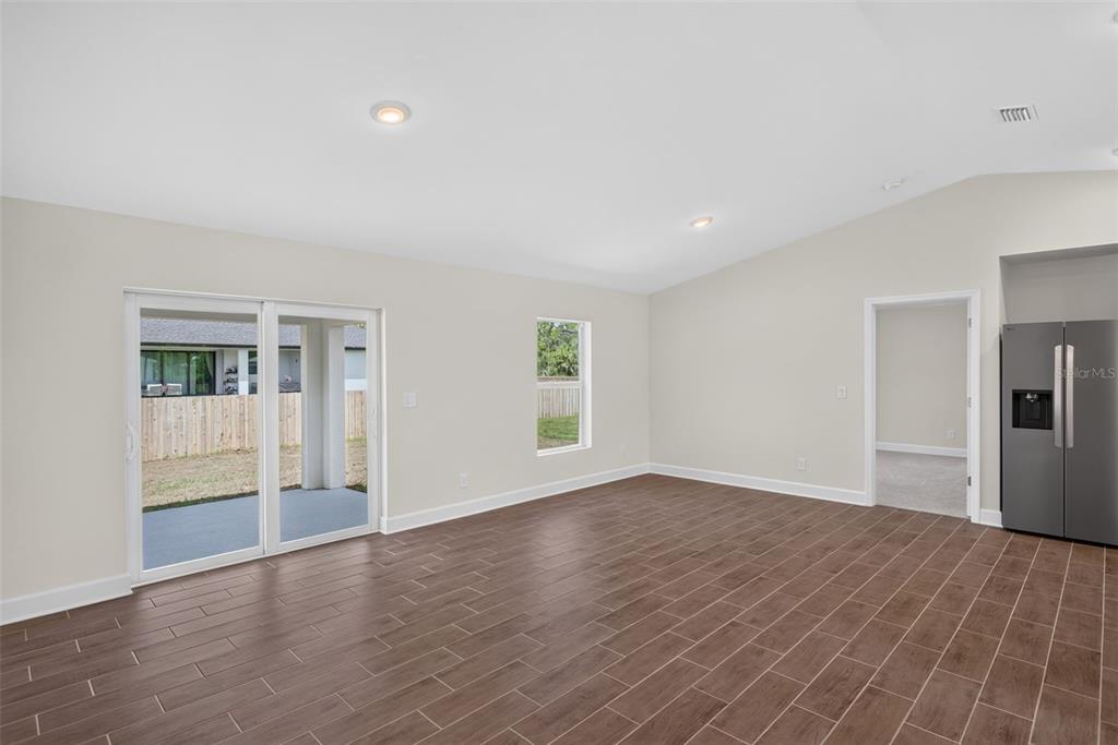 An open living area features wood-look tile flooring, a sliding glass door, and a refrigerator — 3254 PLYMOUTH STREET, PORT CHARLOTTE, FL