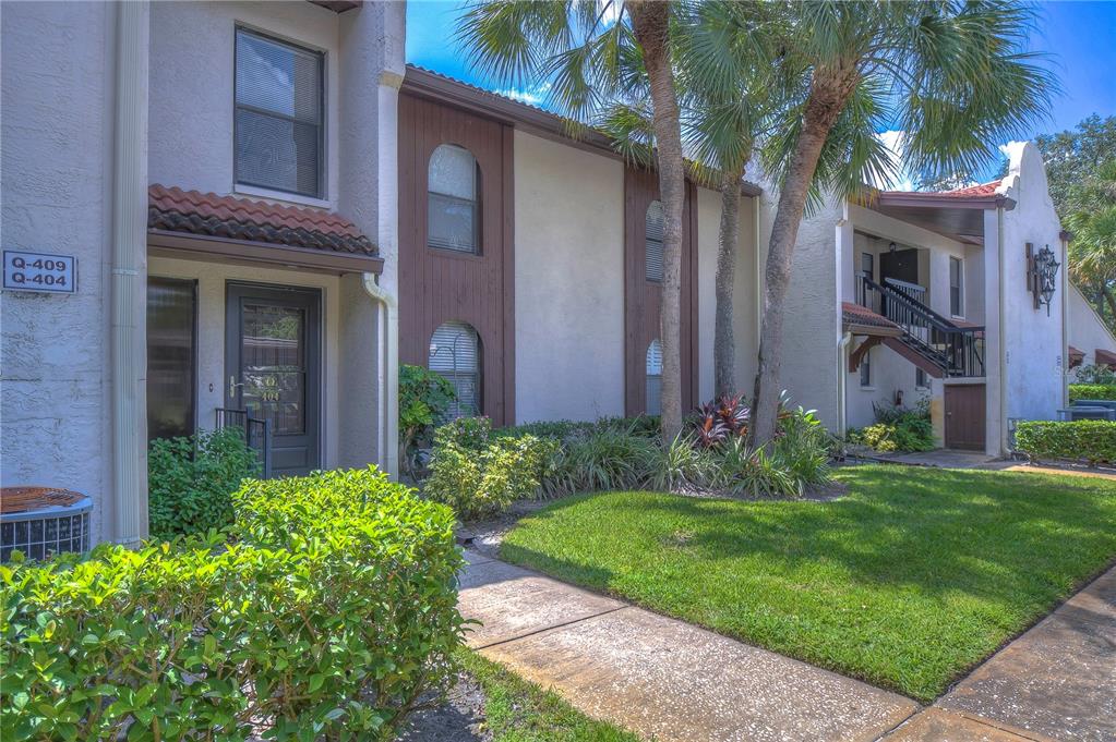 A two-story apartment building exterior features stucco walls, brown trim, and a palm tree — 3505 TARPON WOODS BOULEVARD UNIT Q409, PALM HARBOR, FL