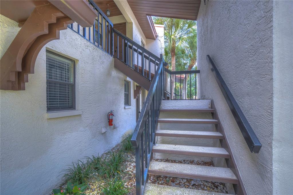 An outdoor staircase leads to an upper-level balcony of a stucco building with palm trees — 3505 TARPON WOODS BOULEVARD UNIT Q409, PALM HARBOR, FL