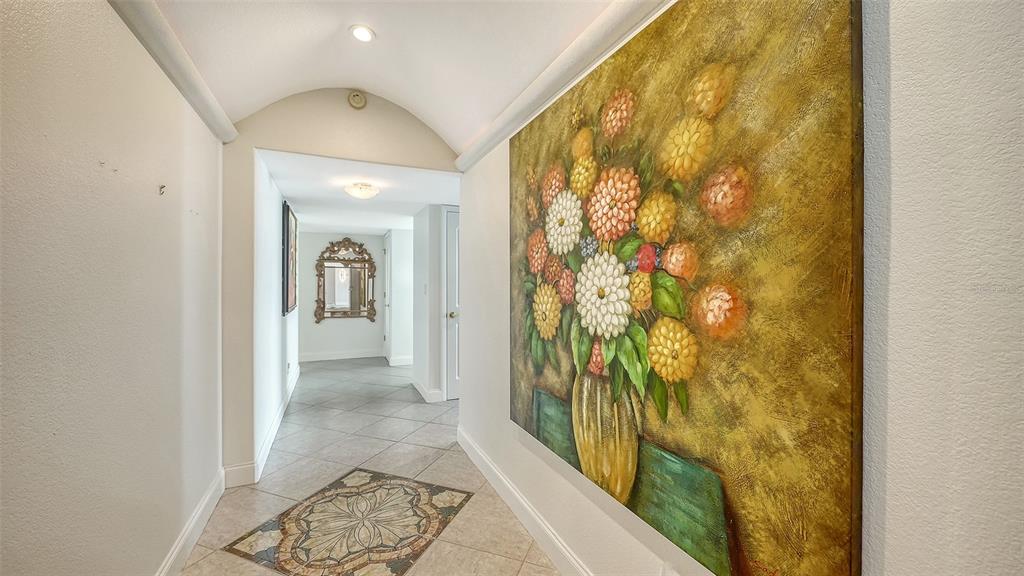 A hallway with a vaulted ceiling, tile flooring, and a large floral painting on the wall — 1111 N GULFSTREAM AVENUE UNIT PH-C, SARASOTA, FL