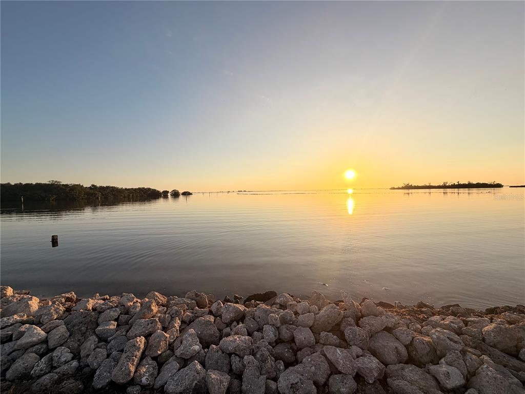 A rocky shoreline overlooks a calm body of water during a bright sunset — 2208 PENNSYLVANIA AVENUE, BRADENTON, FL